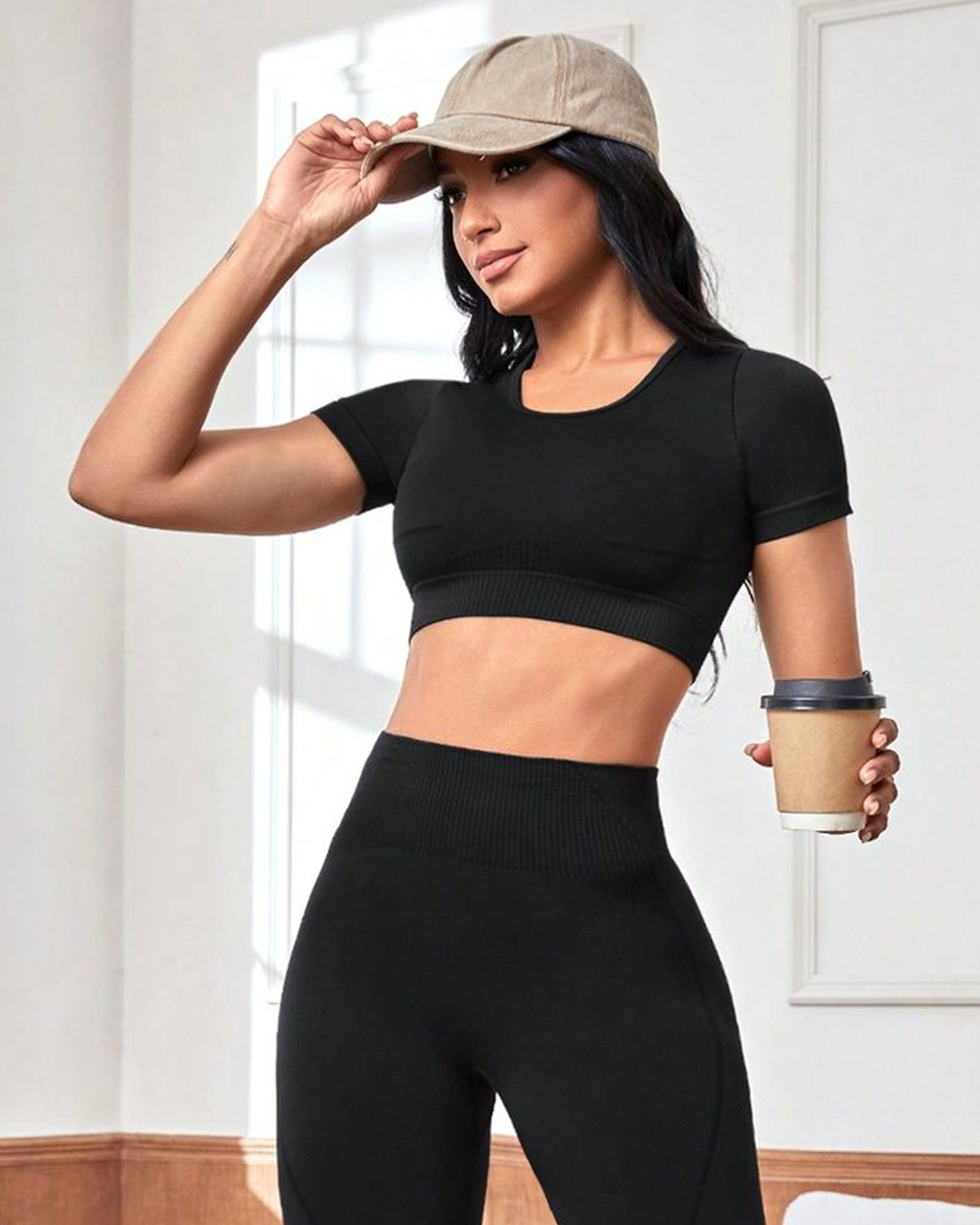 Woman in black athletic wear holding a coffee cup indoors.