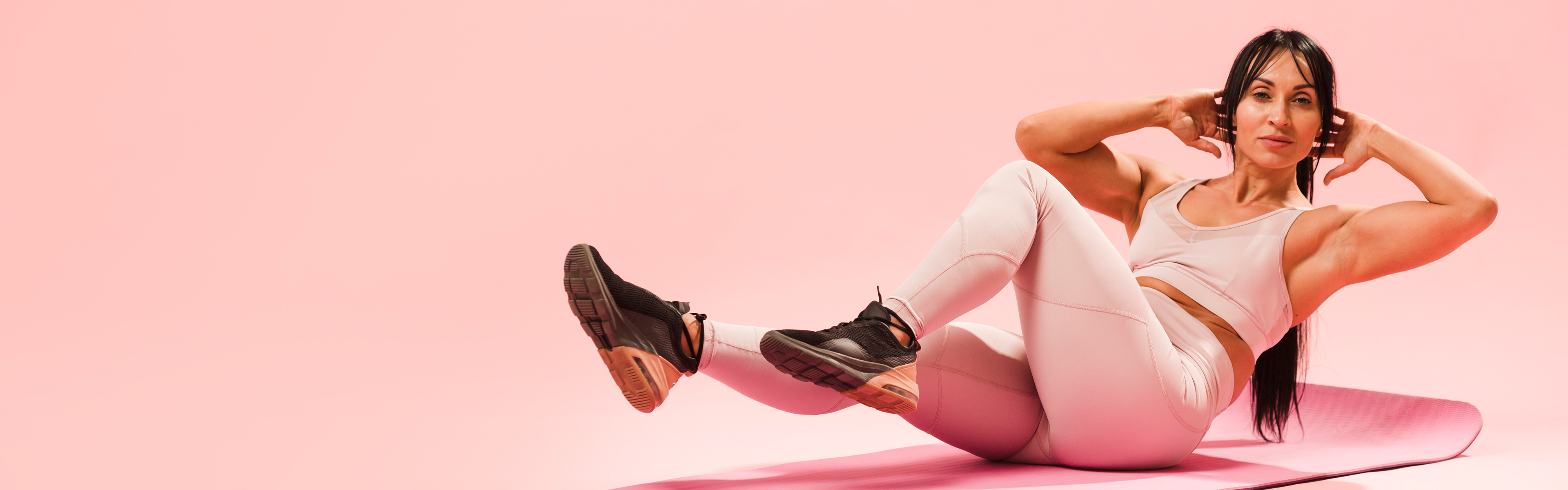 Woman exercising on a pink mat against a pink background